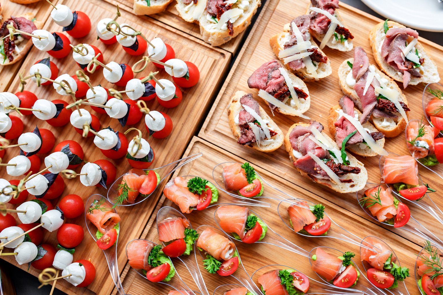 Des planches en bois présentent des brochettes de tomates cerises et mozzarella, des toasts au rôti de bœuf et des cuillères garnies de saumon fumé.